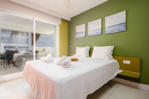 Modern bedroom in Marbella apartment with green walls, double bed, white bedding, and ocean-view artwork above headboard