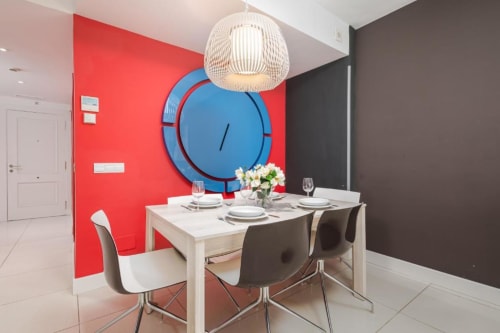Modern dining area at Marbella Home Rentals with red accent wall, blue clock, and contemporary furnishings