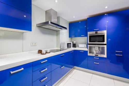 Modern blue kitchen with stainless steel appliances and white countertops in Marbella apartment