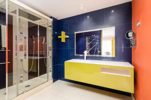 Modern bathroom in Marbella apartment with yellow vanity, navy blue walls, orange accent wall, and walk-in shower