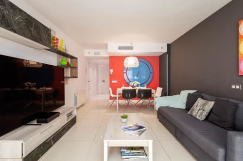 Modern Marbella apartment living room with sofa, dining area, red accent wall, and kitchenette in Puerto Banús