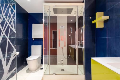 Modern bathroom at Marbella Home Rentals Tembo apartment with blue tile walls, glass shower enclosure, white toilet, and