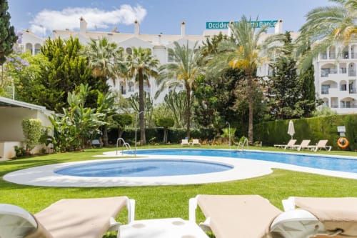 Luxury pool and gardens at Marbella Home Rentals in Puerto Banús, Spain with white apartment buildings and palm trees