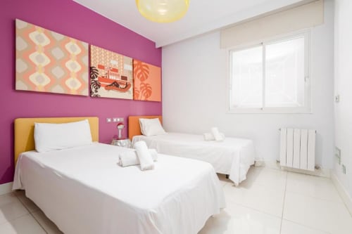 Bright modern twin bedroom in Marbella apartment with vibrant pink walls, white bedding, and colorful artwork