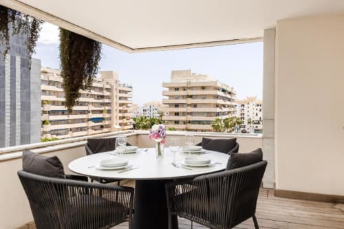 Modern terrace with round dining table and city views of Marbella apartment in Puerto Banús