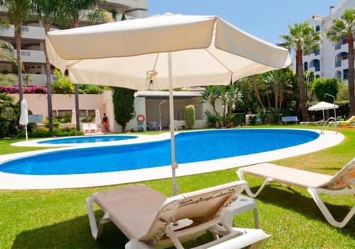 Resort pool with sun loungers and shade umbrella at Marbella Home Rentals, Puerto Banús apartment