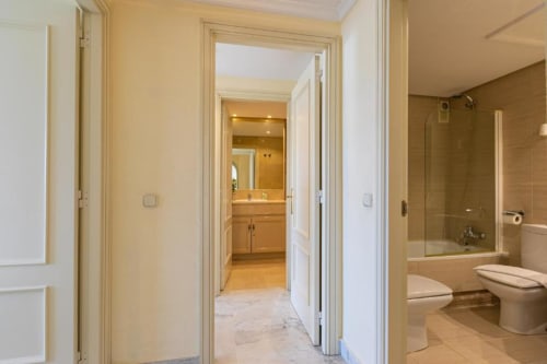 Modern bathroom hallway at Marina Banús apartment, Marbella with marble flooring and access to shower and vanity areas.