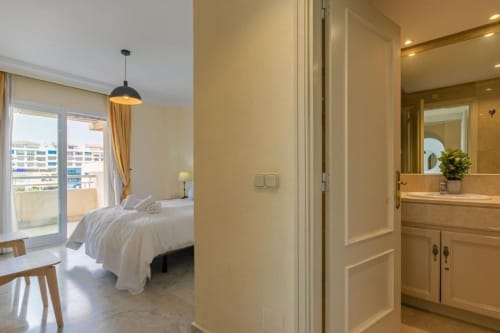 Modern bedroom with bathroom entrance at Marbella Home Rentals Marina Banús apartment, city view balcony visible