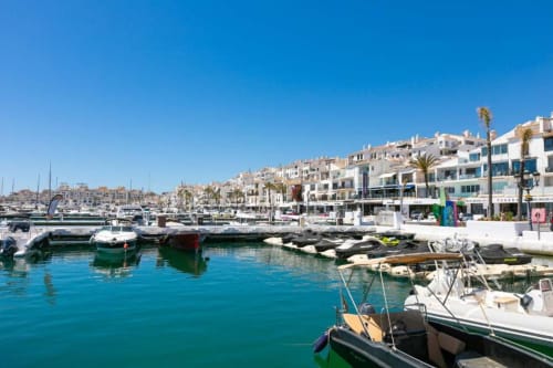 Sunny Puerto Banús marina with moored boats, white apartments, and palm trees in Marbella