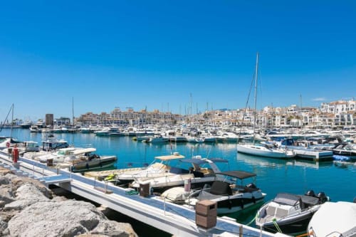Stunning Puerto Banús marina with moored boats and waterfront apartment buildings under clear blue sky