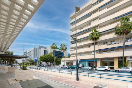 Modern apartment building in Marina Banús, Marbella with palm trees, balconies, and street-level shops