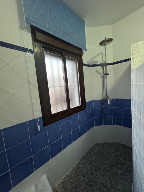 Baño moderno con azulejos azules y crema, ducha tipo lluvia, ventana con marco oscuro en apartamento de Mérida