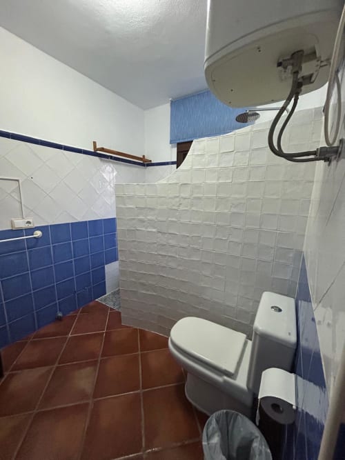 Baño limpio del departamento Gestyp-AT en Mérida con azulejos azules y blancos, piso rojo, inodoro y calentador de agua