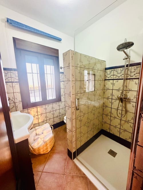 Baño del apartamento Gestyp-AT en Mérida con azulejos beige estampados, ducha integrada, ventana con vistas a la montaña y detalles de madera