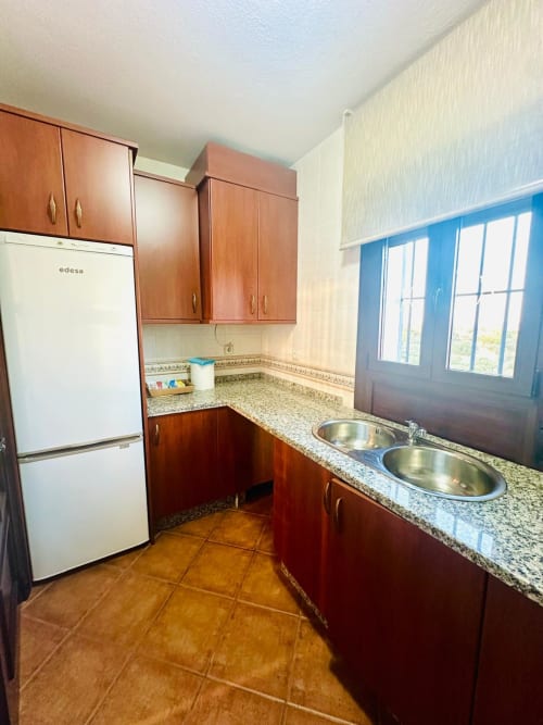 Cocina moderna con gabinetes de madera, encimeras de granito, doble lavamanos y vistas a la montaña en apartamento de Mérida