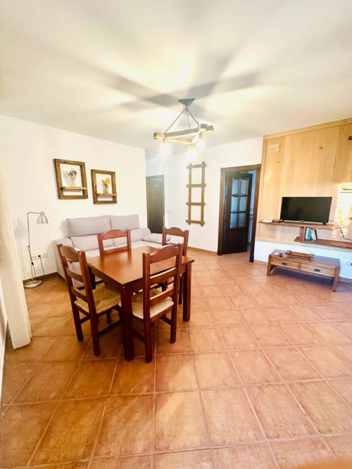 Amplio salón en Mérida con mesa de comedor, sofá beige, TV, muebles de madera y piso de barro cocido.