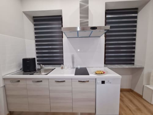 Moderna kuhinja u apartmanu Raymihome Turin s bijeli ormarima, alati od nehrđajućeg čelika, prugastim prozorskim žaluzinama i