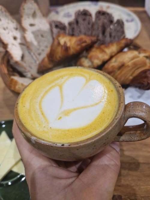 Latte au curcuma doré avec latte art en forme de feuille à la Maisonaurinko B&B à Thénon, France, accompagné de pâtisseries et pain