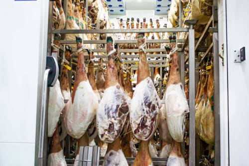 Jamones curados colgados en la sala de almacenamiento climatizada de Gestyp-AT en Mérida, España