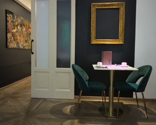 Tavolo da pranzo moderno con sedie in velluto verde, parete scura con cornice dorata a Porta Tosa Milano