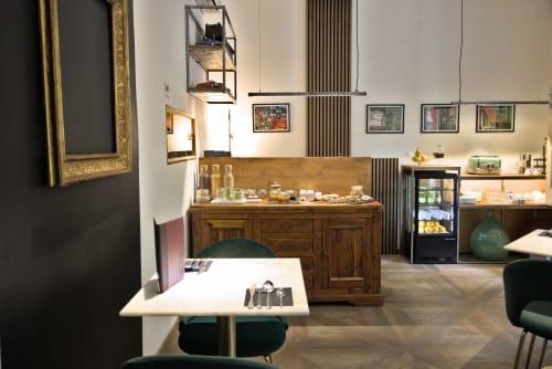 Sala colazione Porta Tosa Milano con credenza in legno, tavolo bianco, sedie verdi e scaffali con prodotti locali