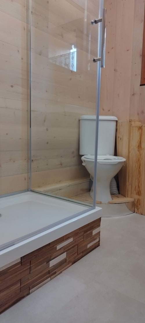 Salle de bain moderne avec douche vitrée, toilettes blanches et murs en bois à L'étape Du Fanfoué à Chamrousse