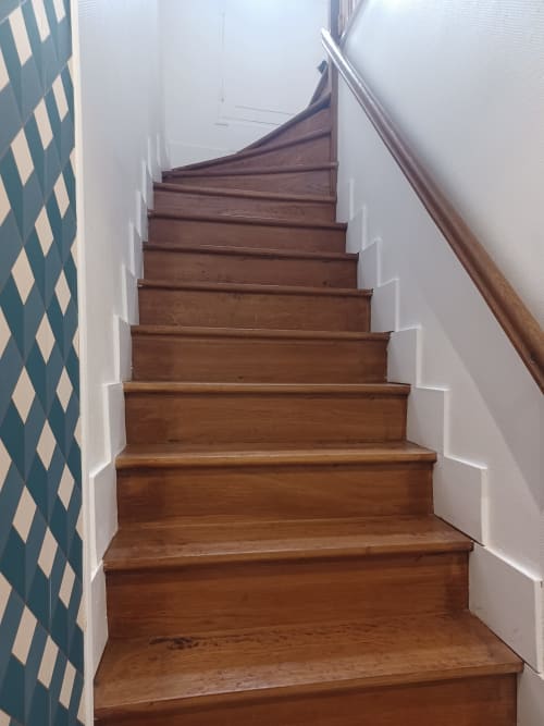 Escalier en bois, murs blancs et papier peint à motifs losanges turquoise au gîte Accolade, Châteaudun