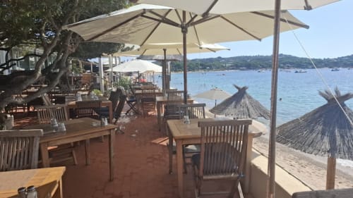 Alma Rossa beachfront restaurant terrace in Lecci with wooden tables, umbrellas, and bay views