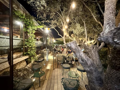 Alma Rossa outdoor terrace at night with wooden deck, vintage tree, bistro seating, and string lights in Lecci