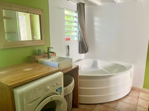 Salle de bain moderne aux Villas aux Antilles avec mur d'accent vert, baignoire d'angle, lavabo, machine à laver et lumière naturelle