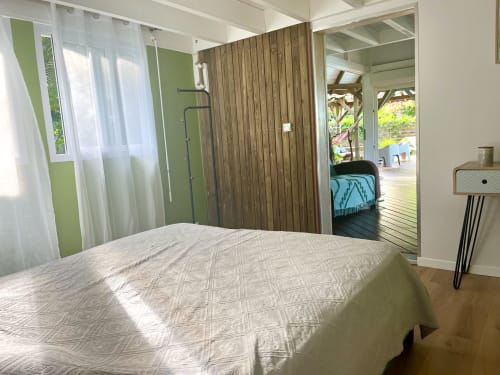 Chambre lumineuse aux Villas aux Antilles avec lit queen-size, mur en bois et vue sur la piscine