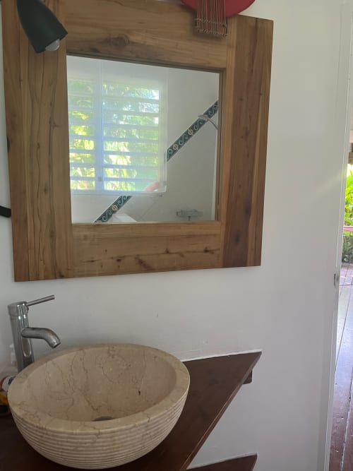 Salle de bain moderne aux Villas aux Antilles avec vasque en pierre ronde, miroir à cadre bois et vue sur jardin tropical.