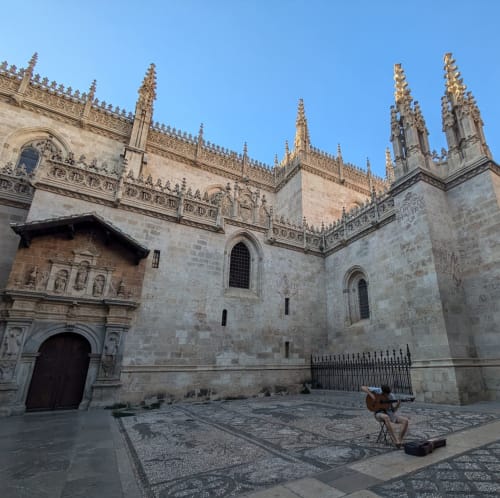 Vista lateral de la Capilla Real de Granada con un músico tocando la guitarra en la plaza frente al edificio histórico.
