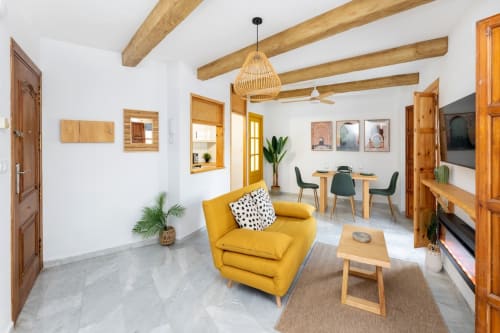 Salón con sofá amarillo, comedor moderno, vigas de madera y decoración acogedora en apartamento turístico de Granada.