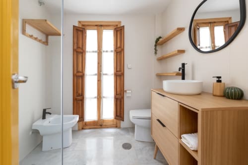Baño moderno con lavabo sobre encimera de madera, ducha y ventana de madera en apartamento turístico de Granada.
