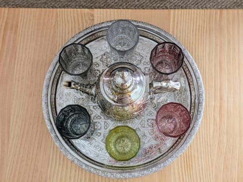 Bandeja decorativa de metal con tetera plateada y vasos de colores sobre una mesa de madera en apartamento turístico.