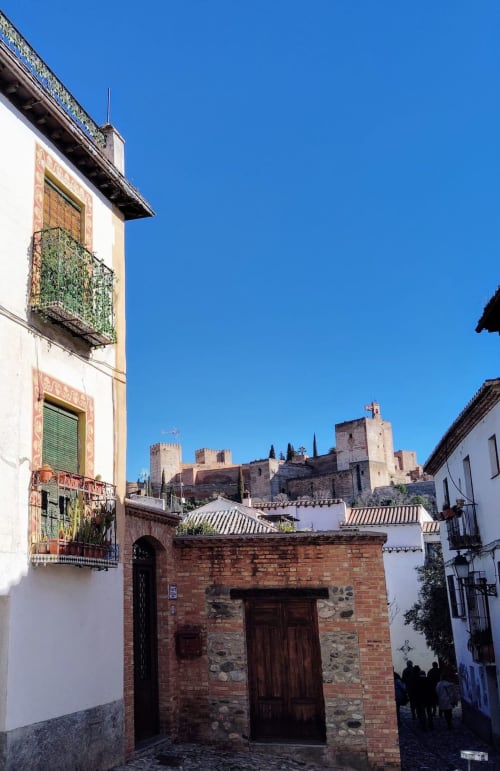 Vista del Albaicín con casas tradicionales y la Alhambra al fondo bajo un cielo azul en Granada.
