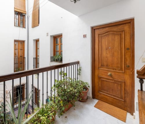 Entrada principal con puerta de madera y plantas decorativas en el balcón interior de apartamento turístico en Granada.