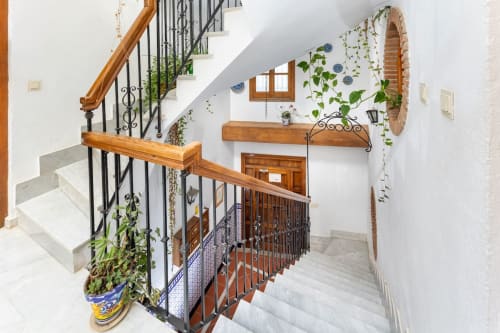 Escalera interior con barandilla de hierro forjado, decoración con plantas y azulejos en apartamento turístico de Granada.
