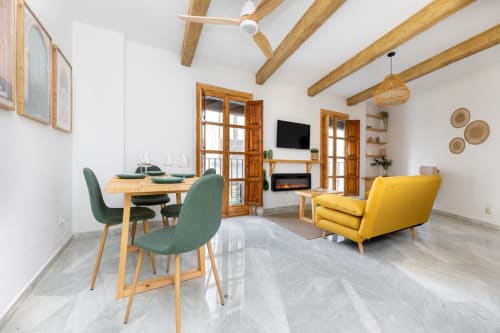 Sala de estar luminosa con sofá amarillo, comedor moderno y decoración de madera en apartamento turístico de Granada.