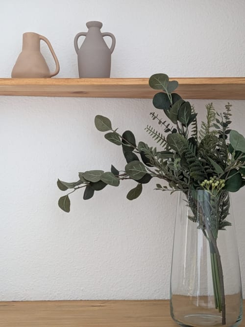 Detalle decorativo con jarrones de cerámica y ramo de hojas verdes en estantería de apartamento turístico en Granada.
