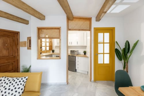 Entrada a cocina moderna con detalles en madera, puerta amarilla y decoración minimalista en apartamento turístico de Granada.