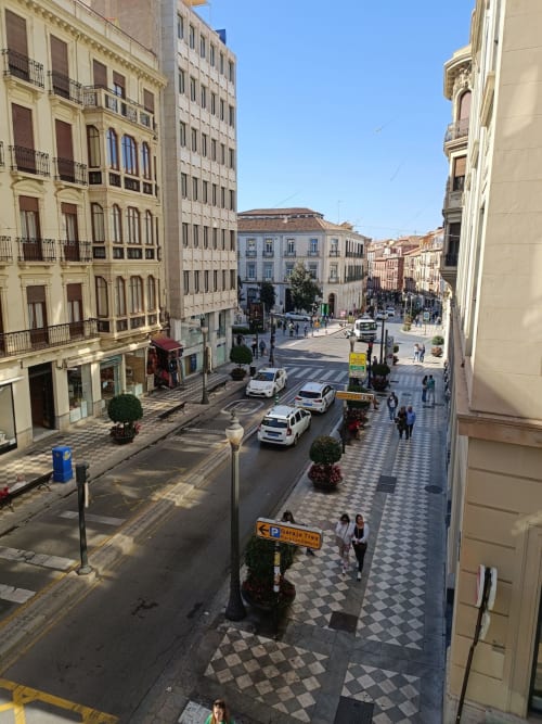 Vista de calle reyes católicos en Granada con edificios clásicos, aceras decoradas y actividad urbana bajo un cielo despejado.