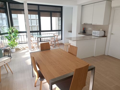 Cocina abierta con comedor de madera y zona luminosa con ventanales en apartamento junto a Plaza Nueva en Granada.