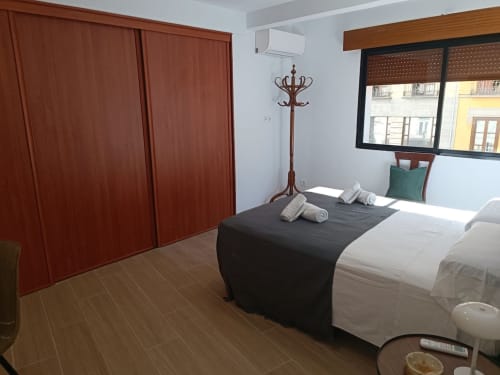 Dormitorio con cama doble, armario de madera, ventana luminosa y decoración sencilla en apartamento céntrico de Granada.