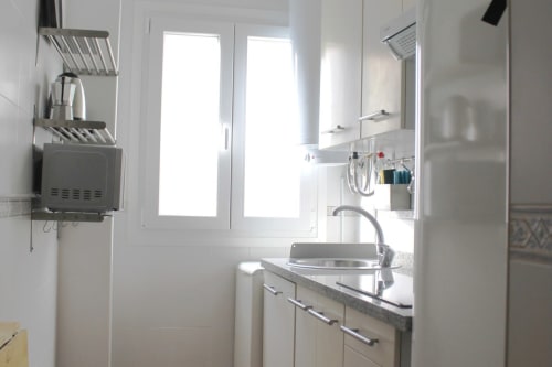 Cocina luminosa y compacta con muebles blancos, fregadero, microondas y cafetera en apartamento turístico de Granada.