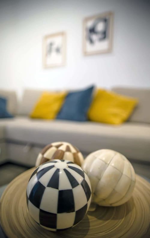 Decoración moderna con esferas geométricas en mesa de centro, sofá beige y cojines amarillos y azules de fondo.