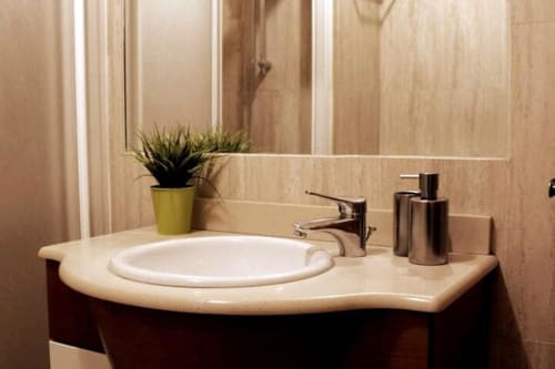 Lavabo moderno con encimera curva, espejo grande, dispensadores metálicos y planta decorativa en baño de apartamento.