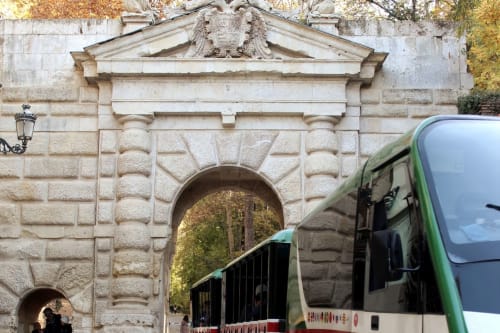 Puerta de las Granadas, entrada histórica a la Alhambra en Granada, con tren turístico en primer plano.