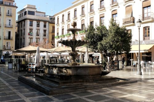 Fuente central en Plaza Nueva, rodeada de terrazas, árboles y edificios históricos en Granada.